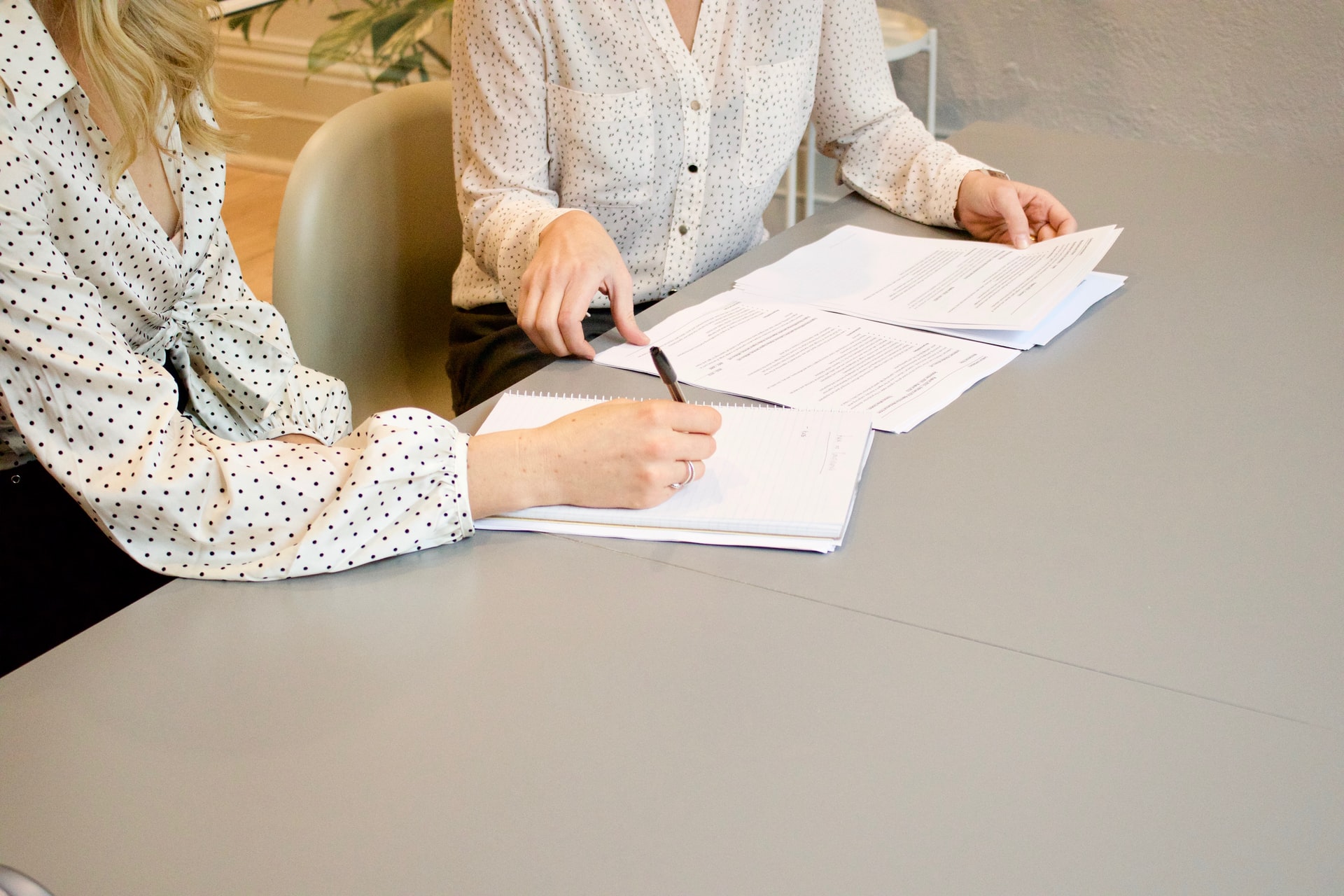 Torsos of two people wearing blouses going over paperwork and pointin