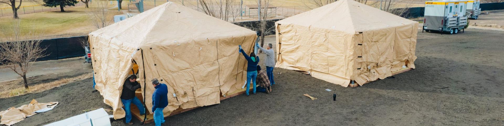 An aerial view of two humanitarian tents placed at the South Railroad Site. Crews place an outer cover on one of the tents.