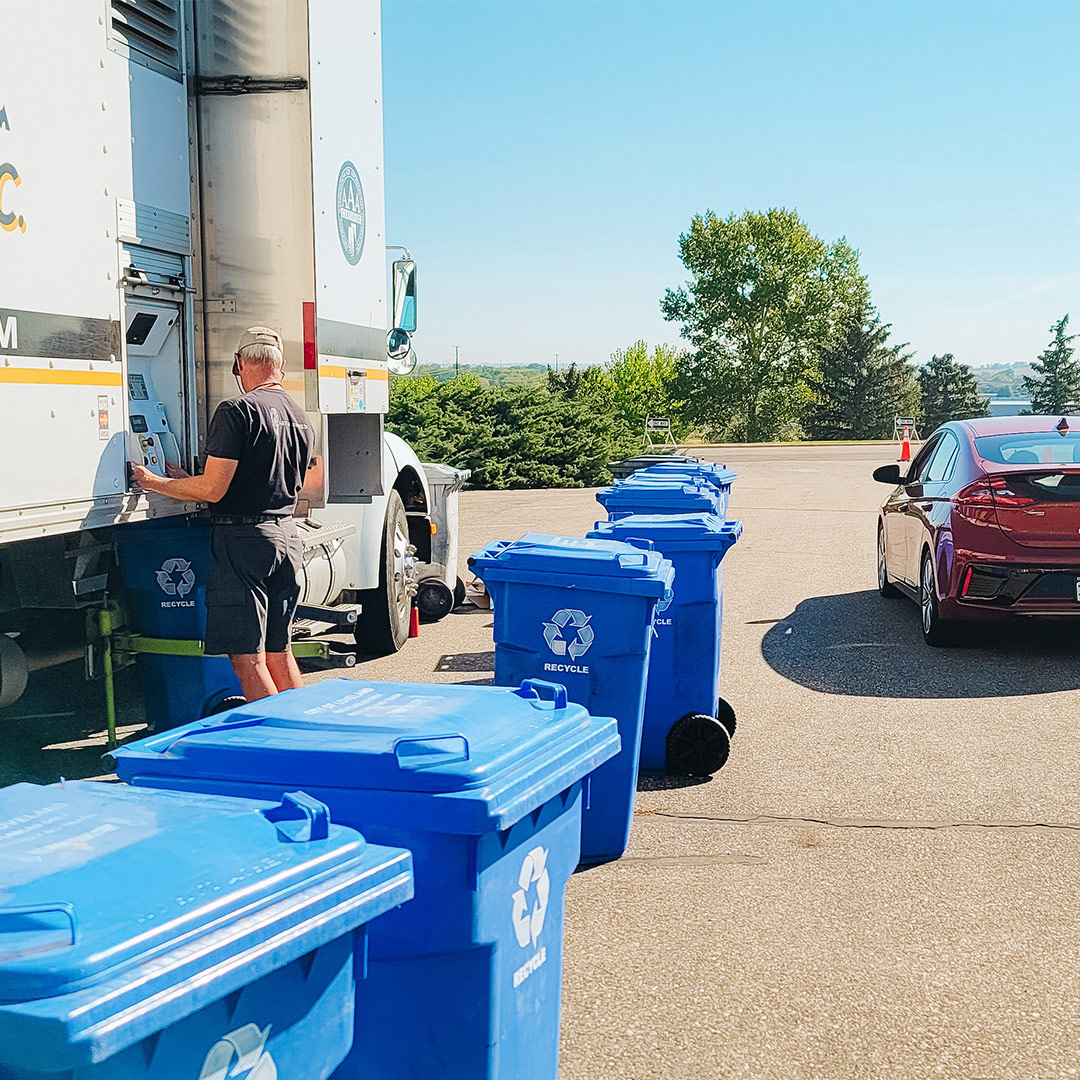 A car parked next to a trailer and several recycling bins.