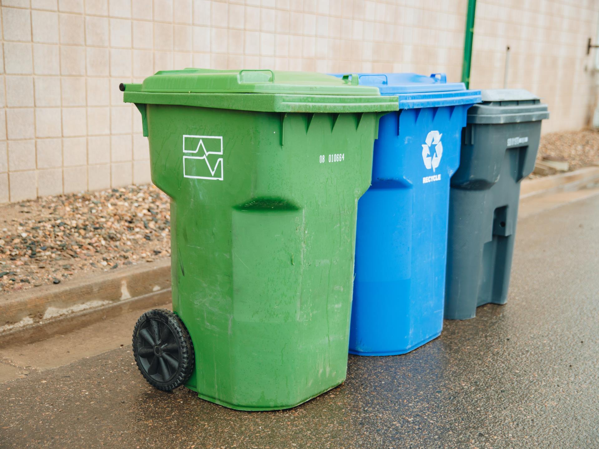 An image of three solid waste carts: a green yard waste cart, a blue recycling cart, and a gray trash cart.