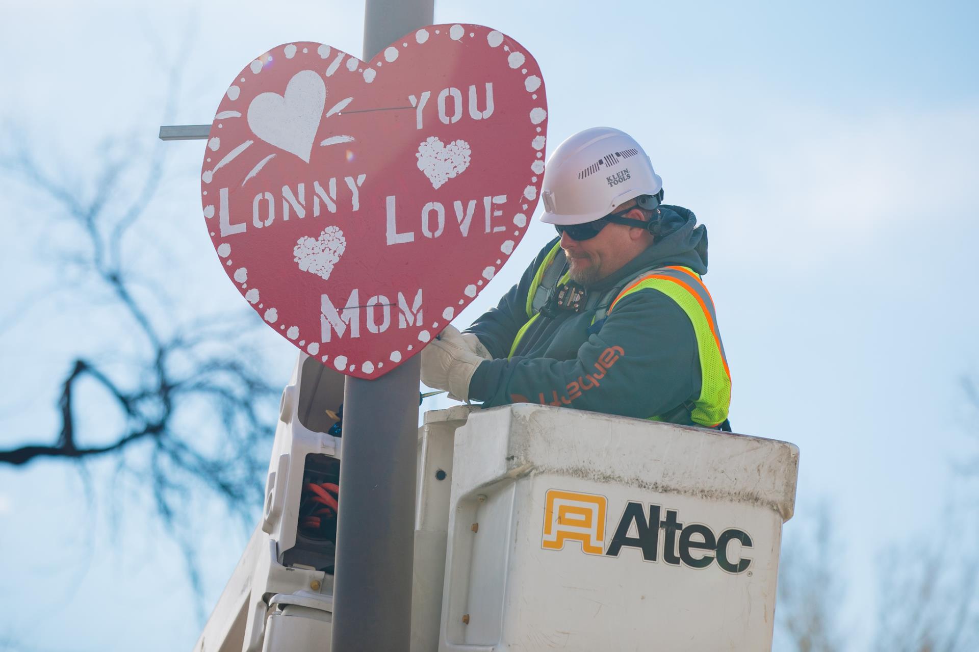 An employee standing in a bucket truck installing a large wooden heart on a light pole.