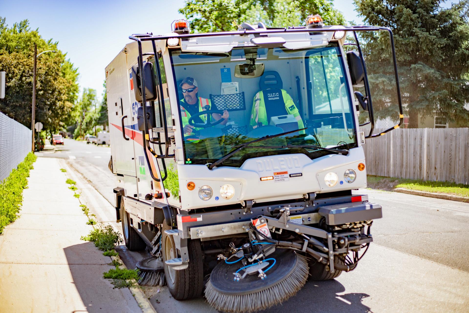 A street sweeping truck sweeps the side of the curb.